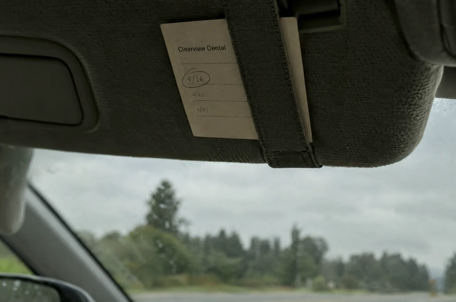 A Clearview Dental appointment card tucked into a car's sun visor strap, with a date circled in pencil.